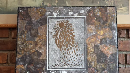 Acrylic artwork featuring a stenciled golden lion profile, framed by a mosaic of dark, earthy tones.
