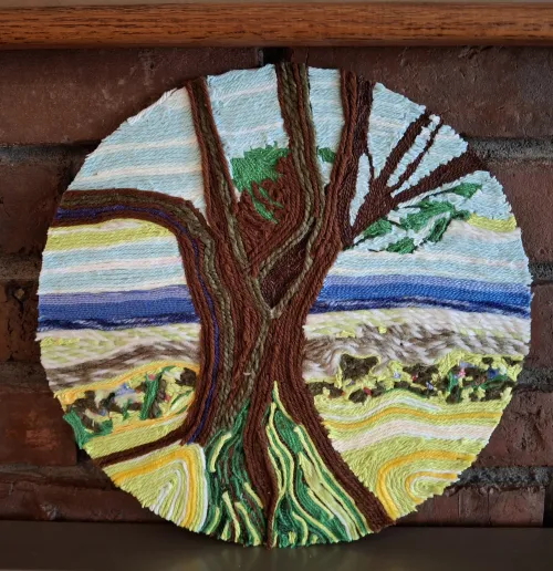 Woven tree in wool wall hanging with brown trunk and blue sky.